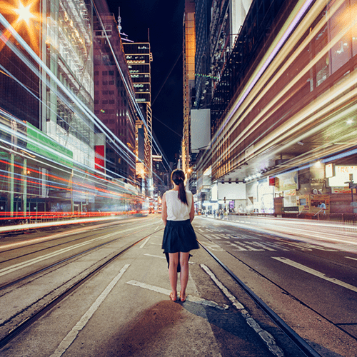 woman standing in city street with blurred lights rushing by